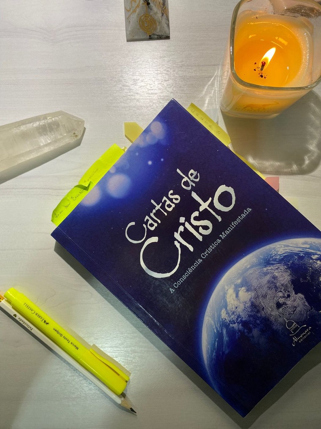 O livro Cartas de Cristo sobre a mesa, ao lado de uma vela acesa e um cristal